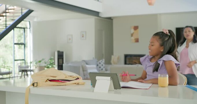 African American mother entering right guiding child for homework at kitchen island with tablet