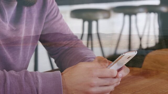 Male patron glancing down and smiling, scrolling phone with thumbs and checking business texts