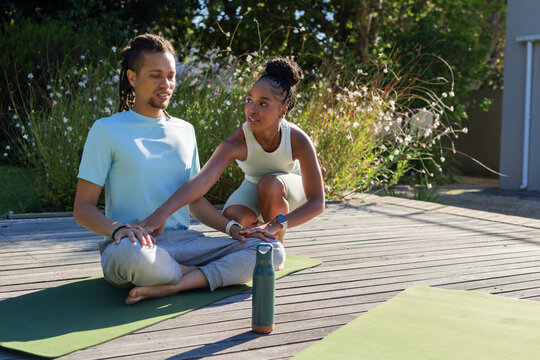 African American couple practicing yoga in workout wear on deck with green mats, smartwatch