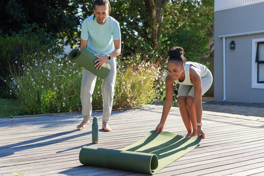 African American couple preparing green mats on deck at home, in sportswear with green water bottle