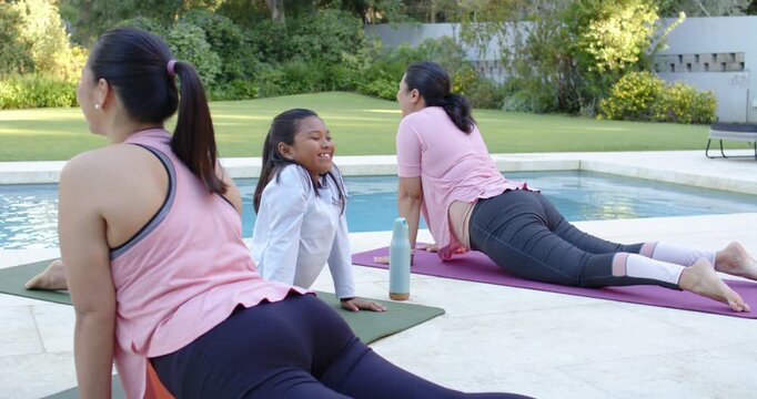 Diverse female friends holding backbend on poolside mats, bottle near, sunny day sparking exercise