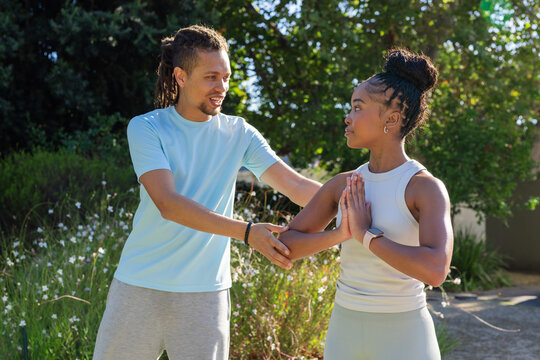 African American fitness partners practicing move on sunlit path, showing smartwatch and bracelet