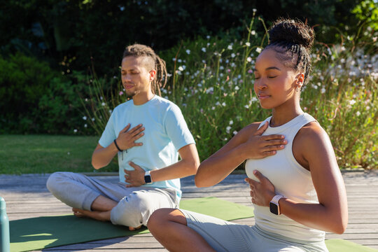 Couple practicing breathing on deck in garden wearing activewear with yoga mats bottle smartwatches
