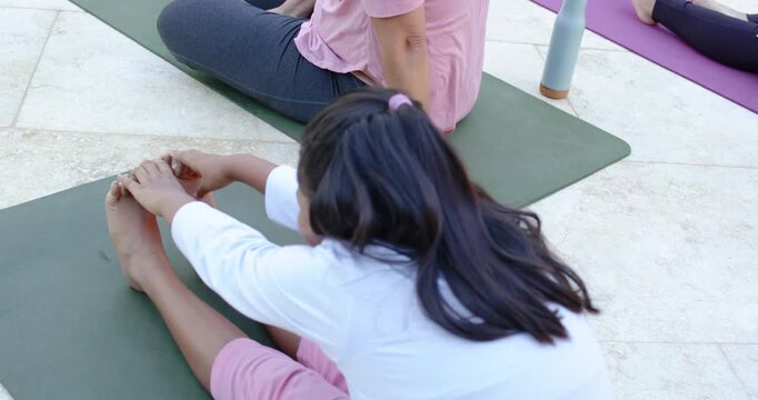 Teen African American girl stretching forward in group class poolside on green mat, grasping toes