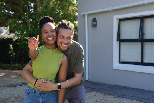 African American couple smiling and holding single house key on red fob in front of house
