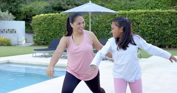 Diverse female mom and daughter practicing wide leg balance step by pool, hugging after mom leads