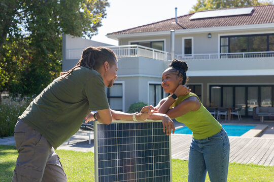 Couple leaning on freestanding solar panel in backyard, chatting by pool and deck