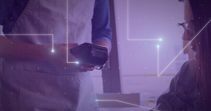 Offering reader, server in apron blue shirt facing customer in denim jacket and glasses at cafe