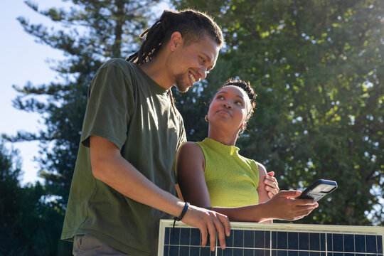 African American couple in summer tees leaning on PV panel checking meter showing wristband in yard