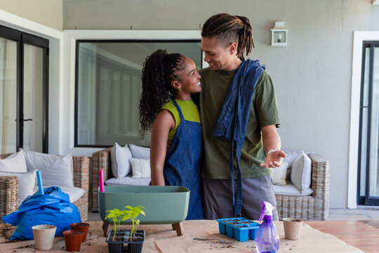African American couple tending seedlings on covered patio at potting table with planter box