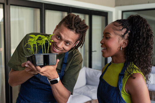 African American couple standing in sunroom wearing blue denim aprons holding black seedling tray