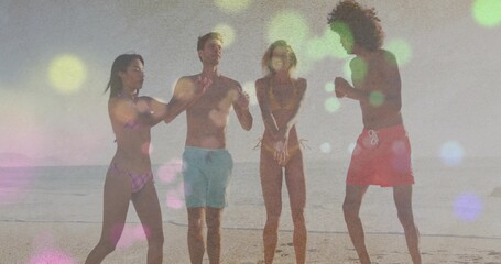 Fototapeta premium Playing group of four friends raising arms and splashing at sandy beach shoreline, swimsuits, bokeh