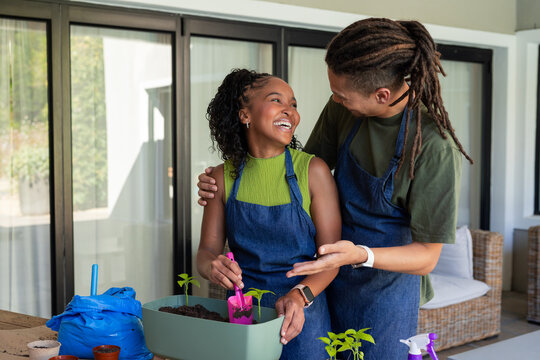 African American couple in blue denim aprons potting plants in planter on patio with pink trowel