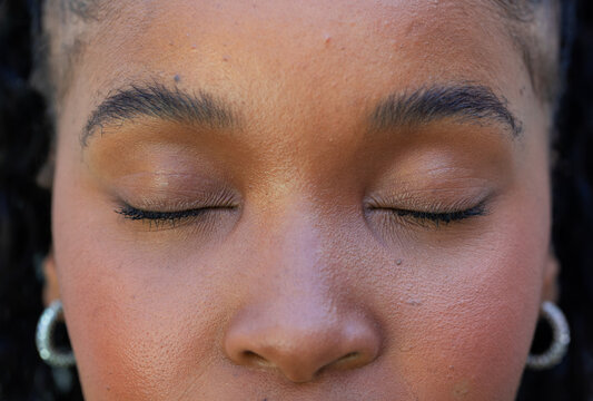 African adult woman in studio closing eyes wearing neutral makeup textured skin silver hoops braids