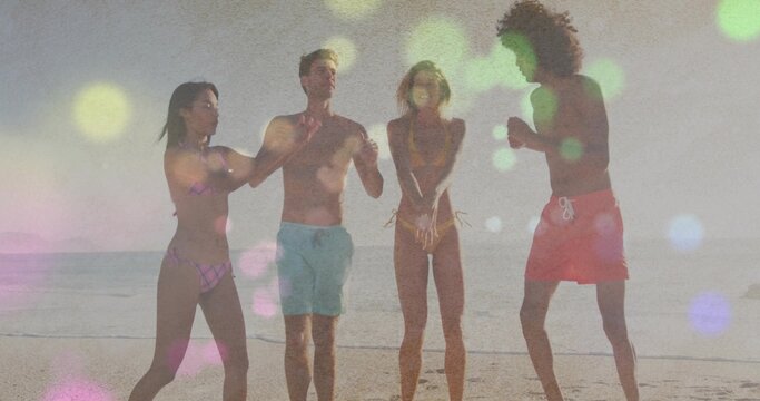 Playing group of four friends raising arms and splashing at sandy beach shoreline, swimsuits, bokeh