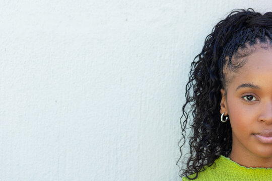 African woman posing on pale textured wall, wearing green sweater and silver hoops, copy space