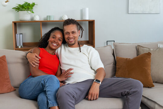 African American couple sitting close on light beige sofa, leaning in and smiling with smartwatch