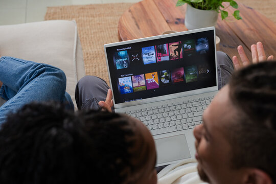 African American couple sitting on sofa, browsing tiles on laptop, coffee table with plant behind