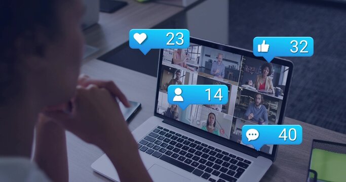 Leaning foreground viewer watching laptop at desk, showing six tiles and reaction icons, phone