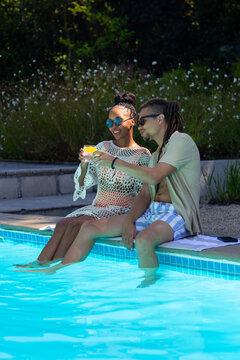African American couple dipping feet in blue pool wearing crochet coverup and holding cocktail