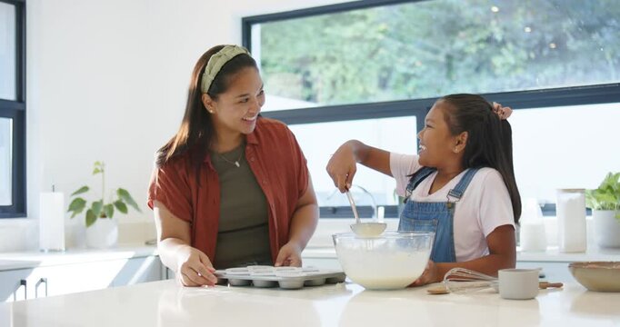 Diverse mom-daughter at counter, mom pointing daughter using whisk, ladling into muffin tin to bake