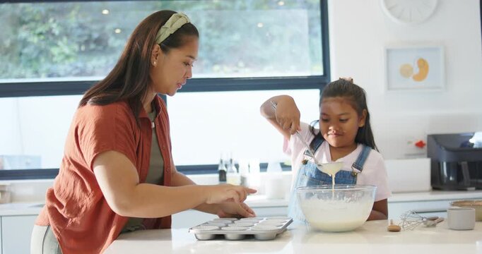 African American mother and child holding muffin tin guiding scooping batter with ladle at counter