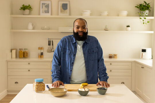 African American man wearing denim shirt standing in home kitchen preparing banana on wooden board