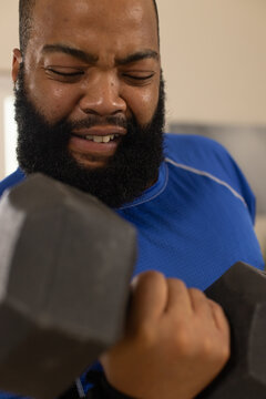 Adult African American man lifting large hex dumbbell at gym, wearing blue athletic shirt