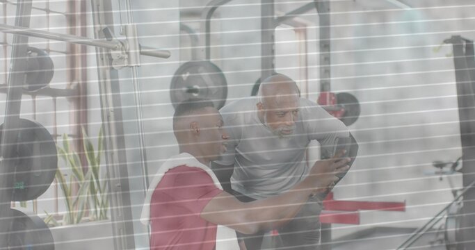 Checking smartphone trainee in red shirt holding towel, trainer in light-gray top leaning at rack