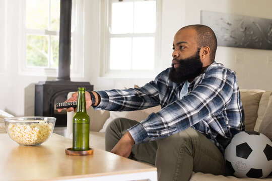 African American adult man leaning reaching for remote watching TV at home with popcorn, copy space