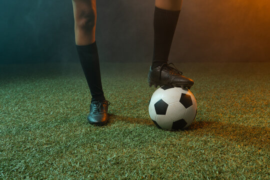 African American female balancing foot on soccer ball on turf in black cleats, knee-high socks