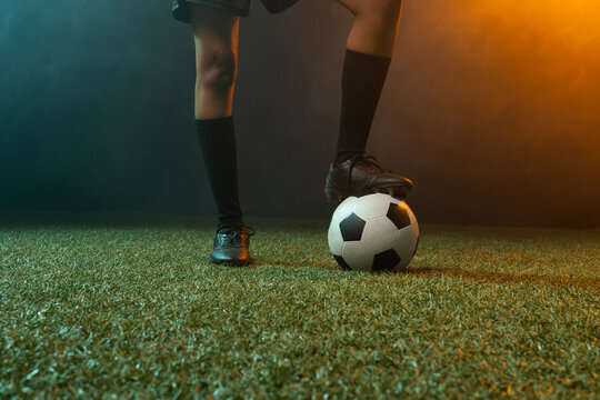 African American woman standing on turf balancing on soccer ball in cleats under colored lights