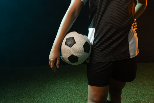 African American woman holding soccer ball at hip on synthetic turf in kit, copy space