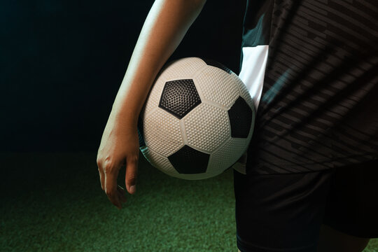 African American adult athlete holding soccer ball at hip on turf, wearing sports jersey and shorts
