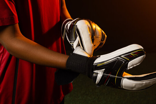 African American woman adjusting white goalkeeper gloves with black wrist strap on green turf
