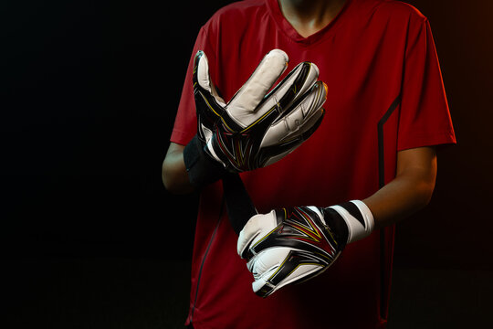 African American female adjusting white goalkeeper glove straps while wearing red jersey in studio
