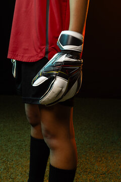 African American woman goalie standing on turf in red jersey holding padded glove with wrist strap