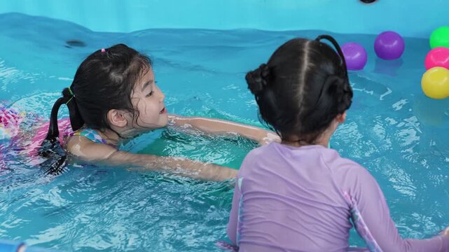 slow motion of happy preschool child girl playing together with her sister in outdoor portable swimming pool in backyard at home