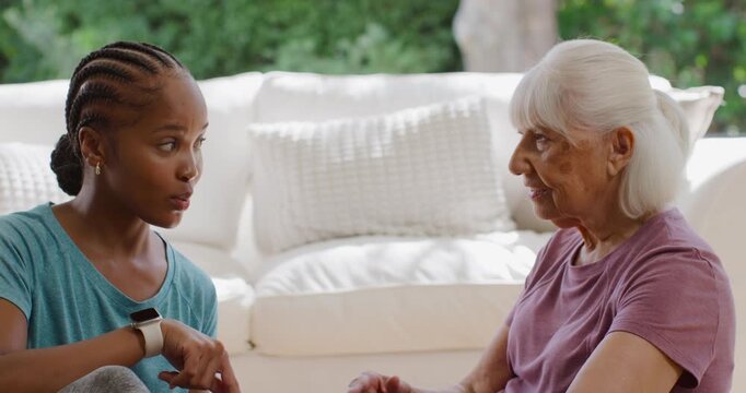 African American woman seeing senior struggling with device, guiding hand, teaching on sofa