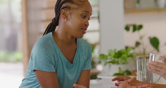 Diverse female pair at counter, senior offering yellow pill bottle, adult inspecting for meds