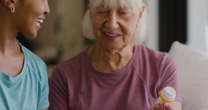 Adult African American woman tapping tablet, nudging Senior woman confirming pill bottle on couch