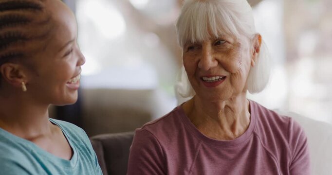Grandmother and granddaughter reminiscing about family with grandmother speaking softly on sofa
