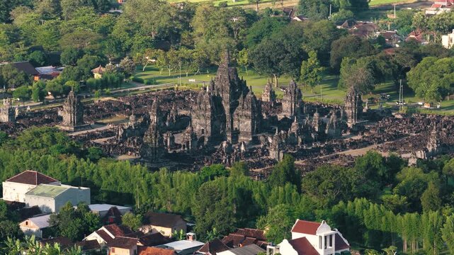 Aerial view of Prambanan Temple complex with ancient stone spires surrounded by lush green trees and village rooftops in Kecamatan Prambanan, Daerah Istimewa Yogya, Indonesia.