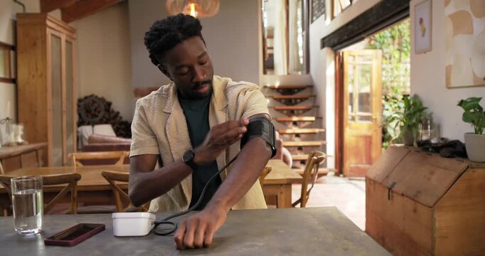 African American man rolling sleeve fitting cuff joining tubing to white unit at home monitoring BP