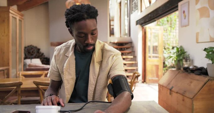 African American man placing cuff, operating monitor, checking blood pressure at dining table