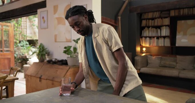 African American man entering home drinking water sitting at table opening white case testing parts