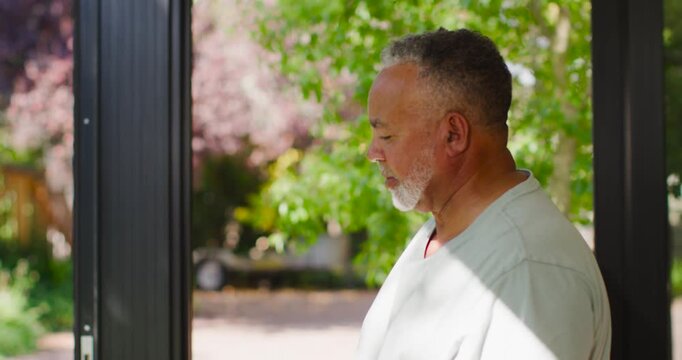 African American senior man standing on porch, dappled sun on face, scanning yard and smiling