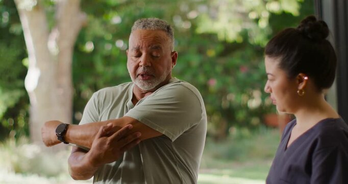 Senior African American man feeling shoulder pain doing arm stretch on patio while Asian PT guiding