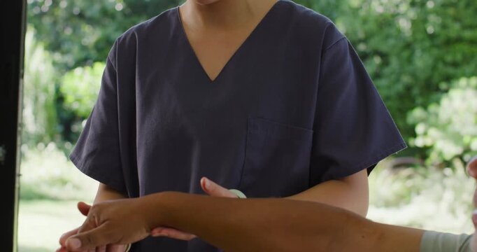 Asian woman in scrubs palpating patient forearm as man extending arm at window, checking alignment
