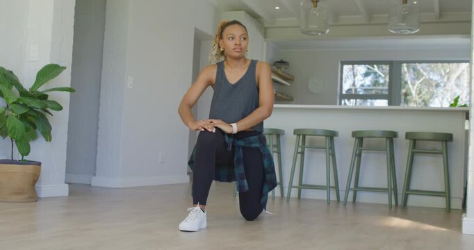 African American woman moving from deep lunge to hamstring fold in kitchen, deepening stretch